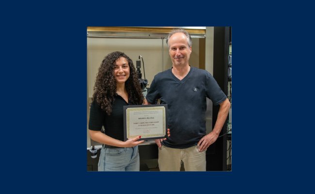 woman with dark hair holding a plaque standing next to man in dark blue shirt