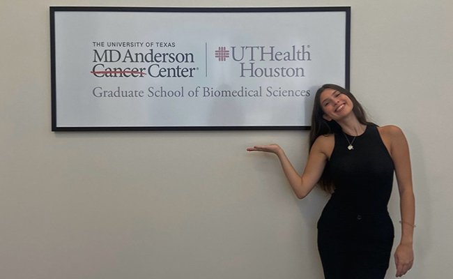 dark-haired woman smiling by a sign