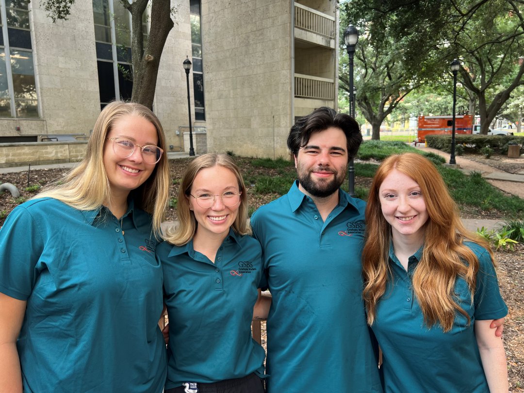 Four students in teal shirts standing together smiling