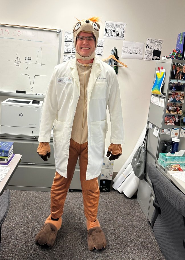 Harlan standing in the office posing in his Halloween costume in 2024.