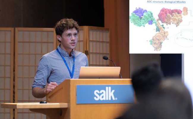 High standing at the podium presenting his research at the Salk Institute for Biological Studies 2025 Discover Symposium.