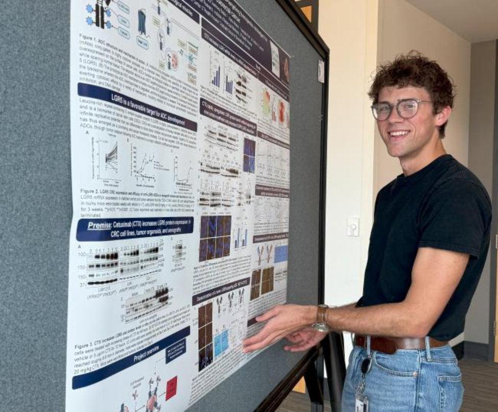 Peyton standing by his poster at Graduate Student Research Day 2025.