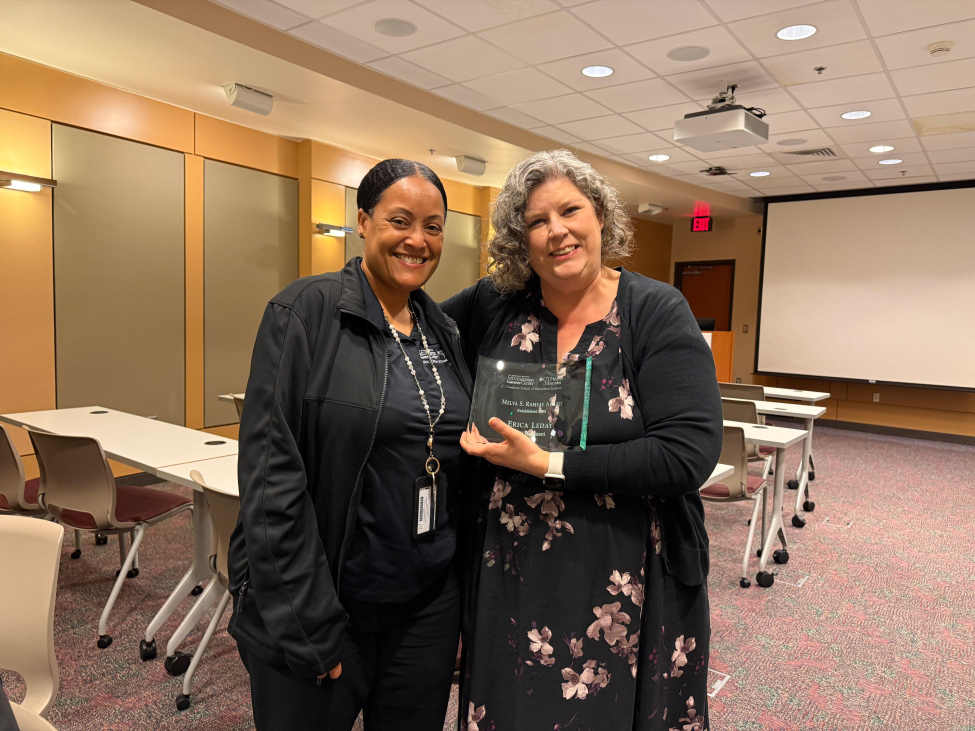 Leday standing next to Karen Weinberg, who is holding Leday's award plaque.